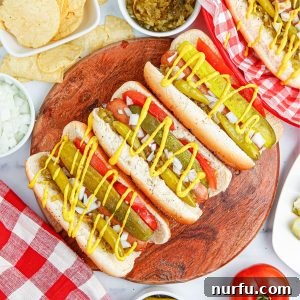 A beautifully arranged Chicago style hot dog on a plate, garnished with its signature toppings like pickle, tomato, sport peppers, and mustard.