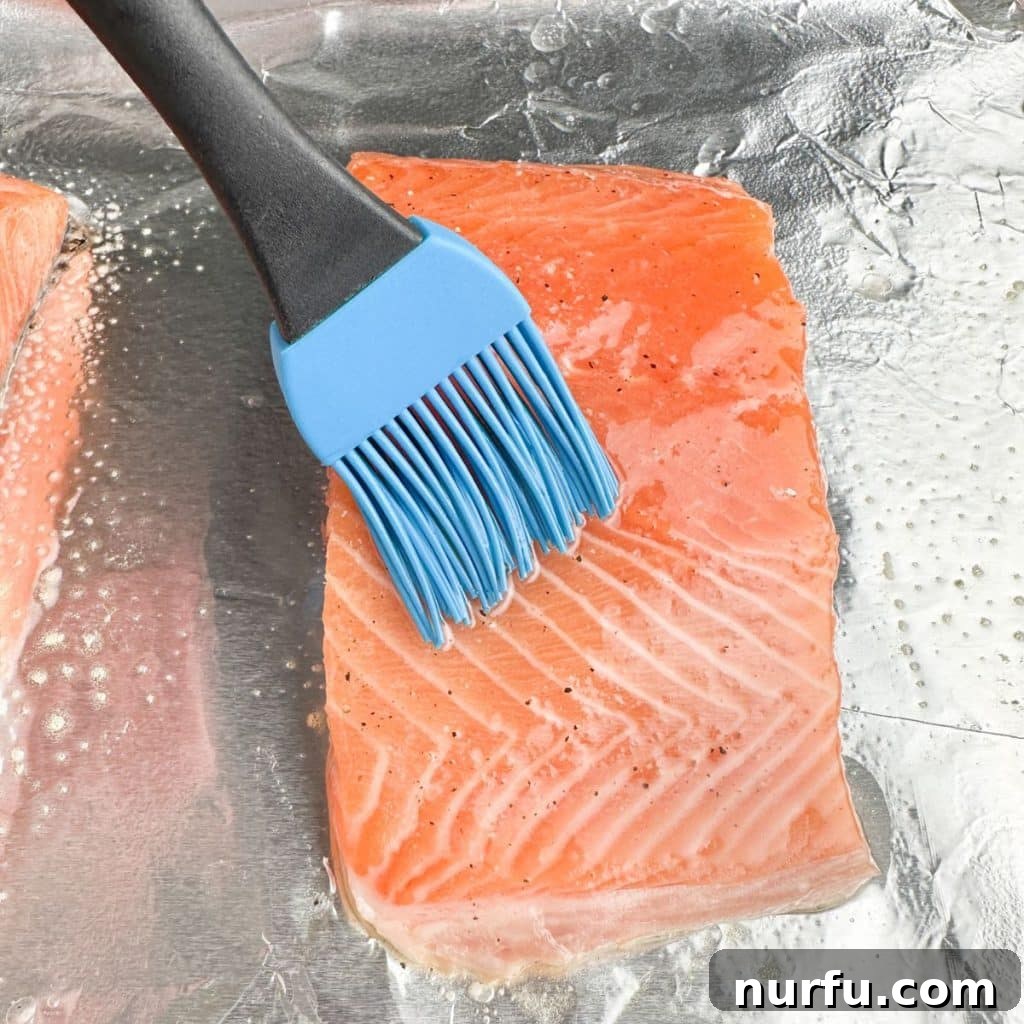 Salmon fillets arranged on foil, being brushed with olive oil and seasoning mixture.
