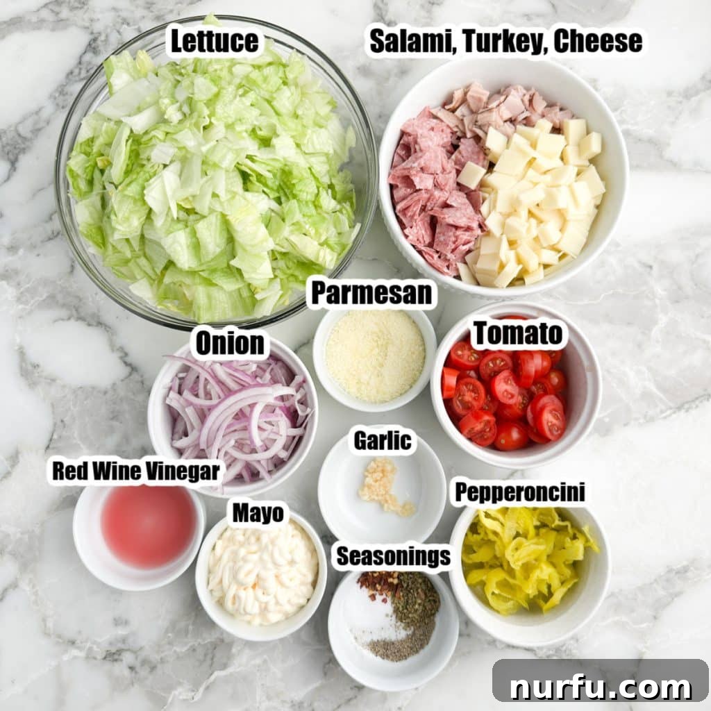 A glass bowl showcasing the individual ingredients of the Grinder Salad: crisp lettuce, sliced red onions, vibrant tomatoes, various deli meats, cheese, and a dollop of mayonnaise ready to be mixed.