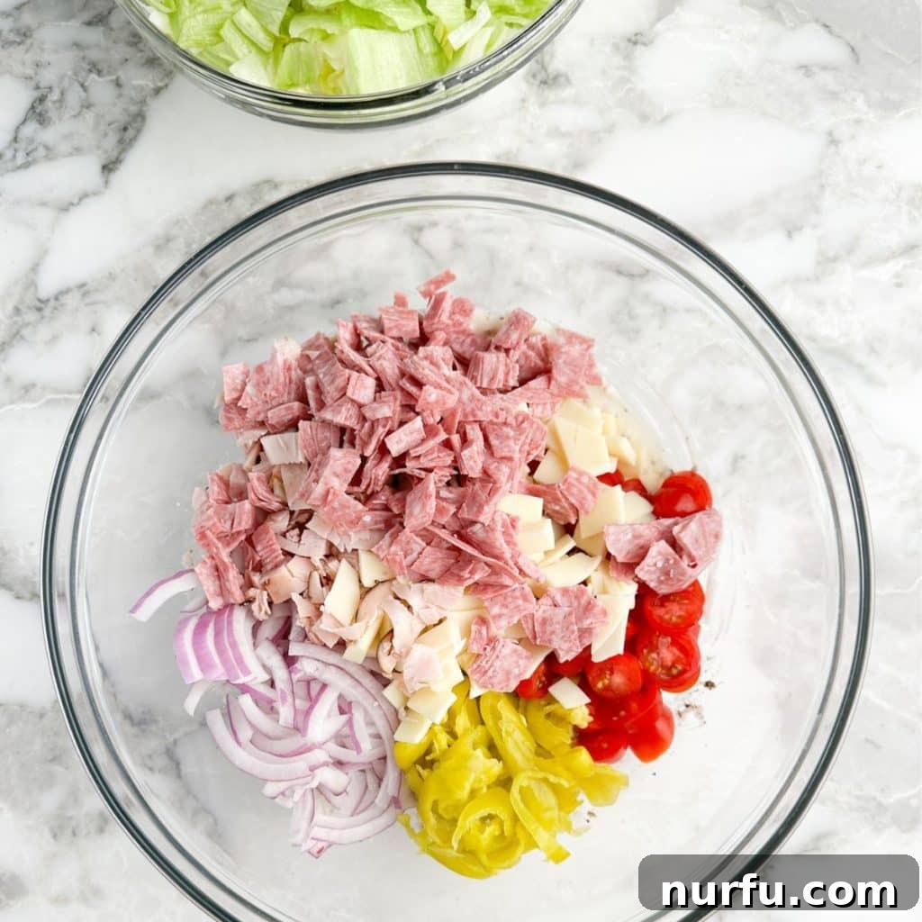 A large bowl filled with an inviting mix of chopped deli meats, onions, tomatoes, cheese, and peppers, waiting to be combined with lettuce and dressing for the Grinder Salad.