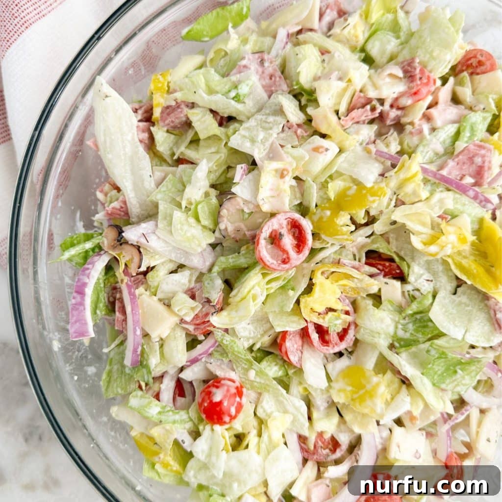 A beautifully chopped Grinder Salad served in a clear glass bowl, showcasing the vibrant colors and appealing textures of the fresh ingredients and creamy dressing.