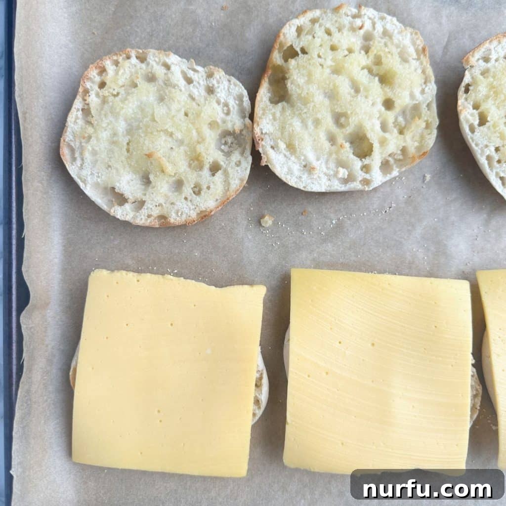 The Ultimate Homemade Breakfast Sausage Muffin 4 A toasted English muffin half with a slice of American cheese melting on top, placed on a baking sheet.