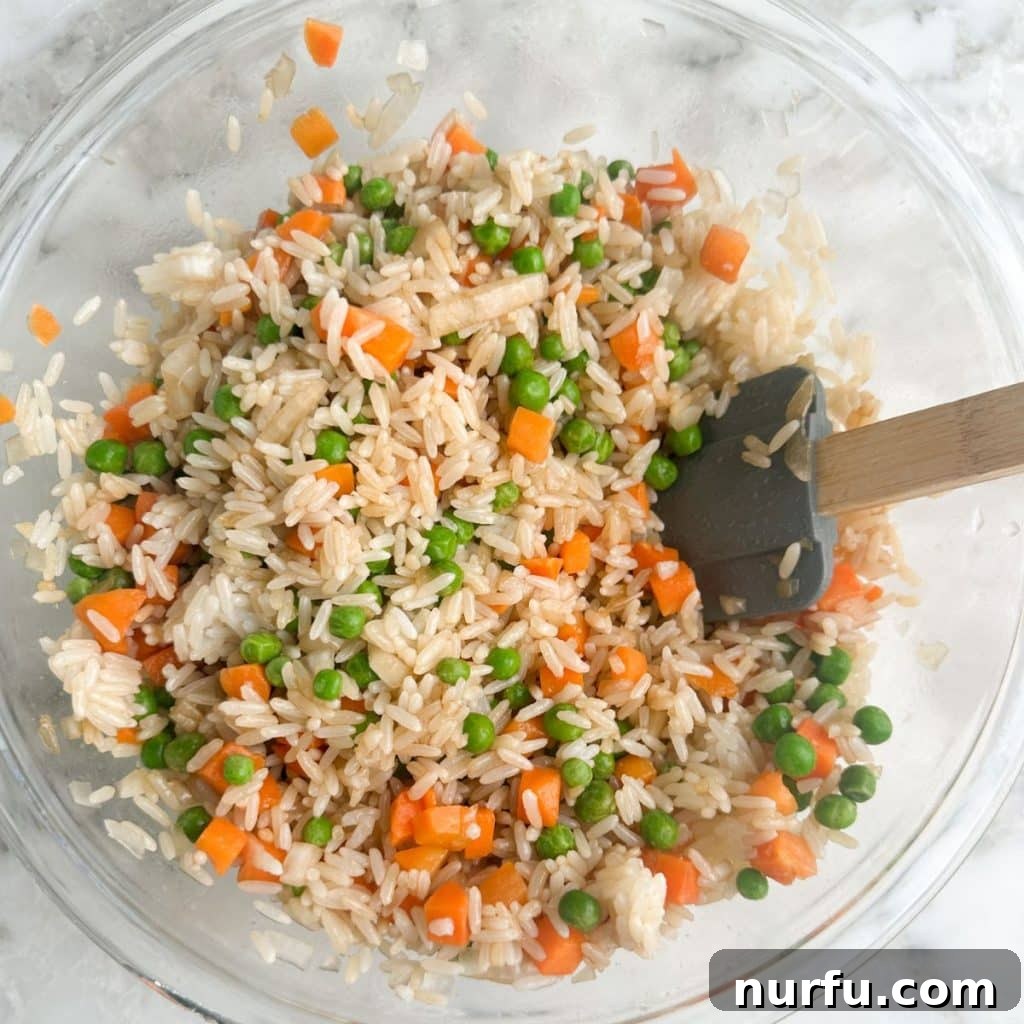 Sheet Pan Fried Rice Magic 5 Cooked rice with carrots and peas seasoned with soy sauce and oil in a bowl, stirred and ready for baking.