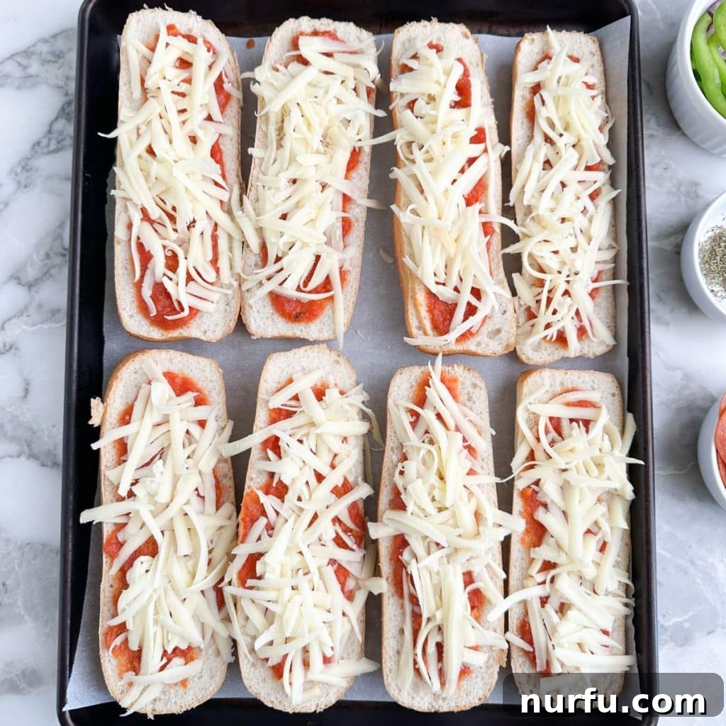 Ultimate Pizza Sub Melts 4 Split sub rolls on a baking pan, each half generously spread with bright red pizza sauce and covered with a thick layer of shredded mozzarella cheese, ready for toppings and baking.