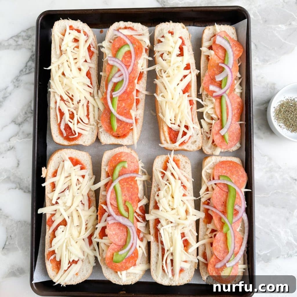 Ultimate Pizza Sub Melts 5 Assembled pizza subs on a baking pan, vibrant with toppings like pepperoni, bell peppers, and onions over a bed of melted cheese and sauce, seasoned with Italian herbs, and ready to be baked to perfection.