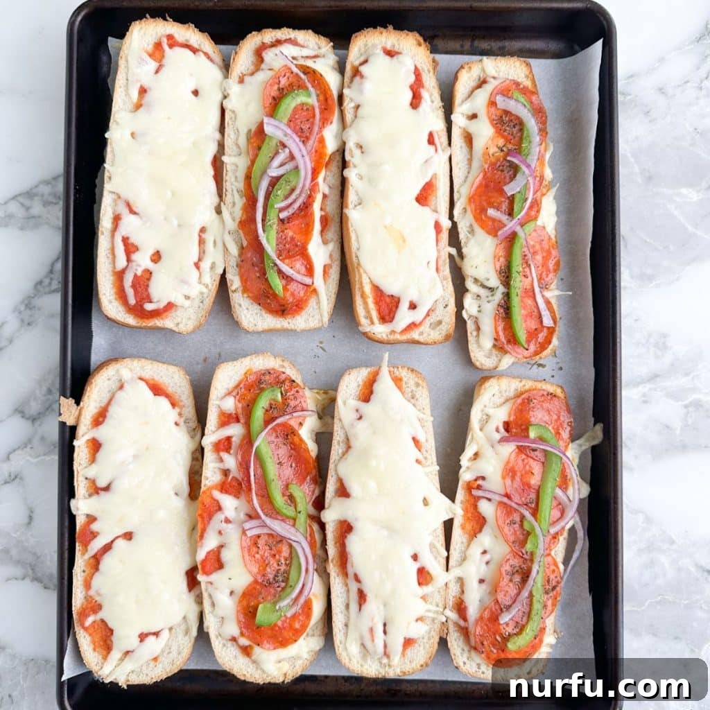 Ultimate Pizza Sub Melts 6 Freshly baked pizza sandwiches on a baking pan, golden brown and bubbling with melted cheese and pepperoni. The subs are perfectly toasted, indicating they are hot and ready to be served.