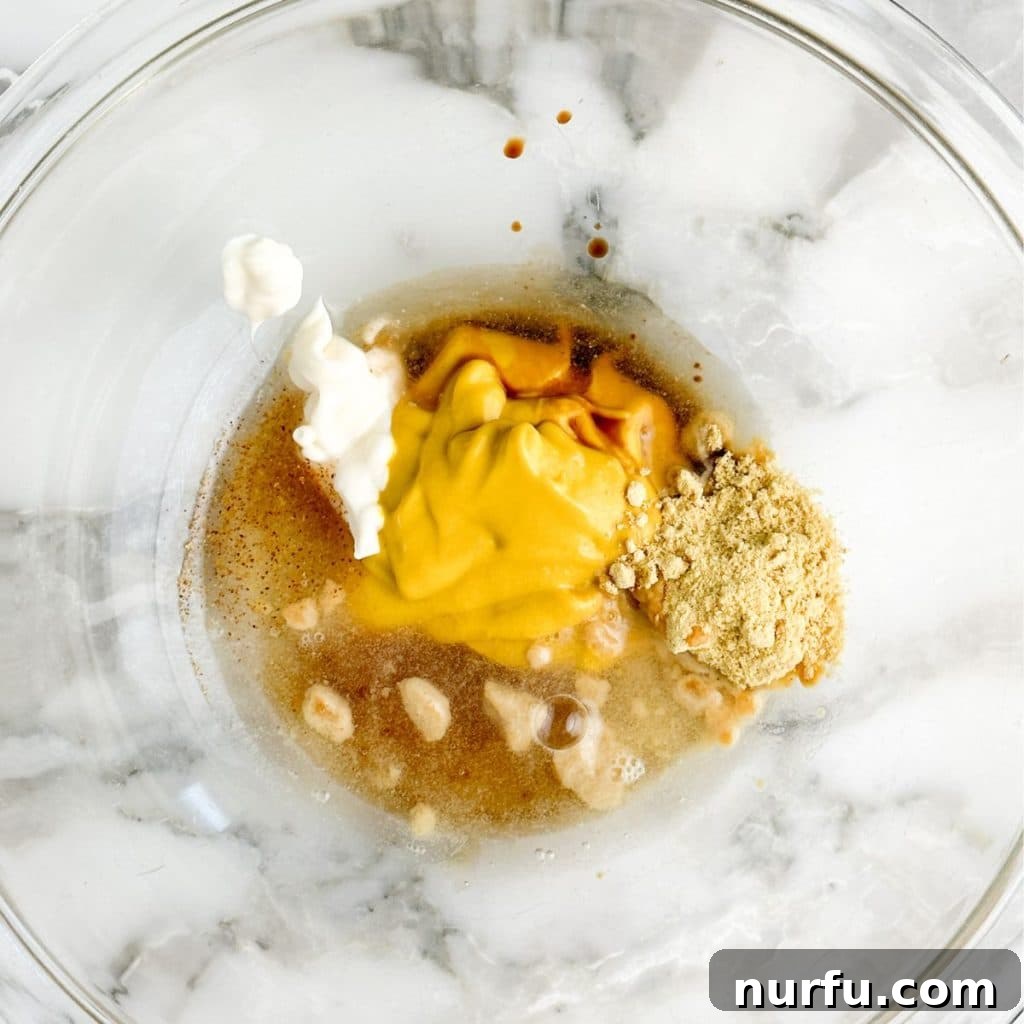 McDonald's Hot Mustard Sauce Copycat Recipe 4 A bowl filled with a creamy yellow mixture of mustard, mayonnaise, and other seasonings, being whisked to combine.