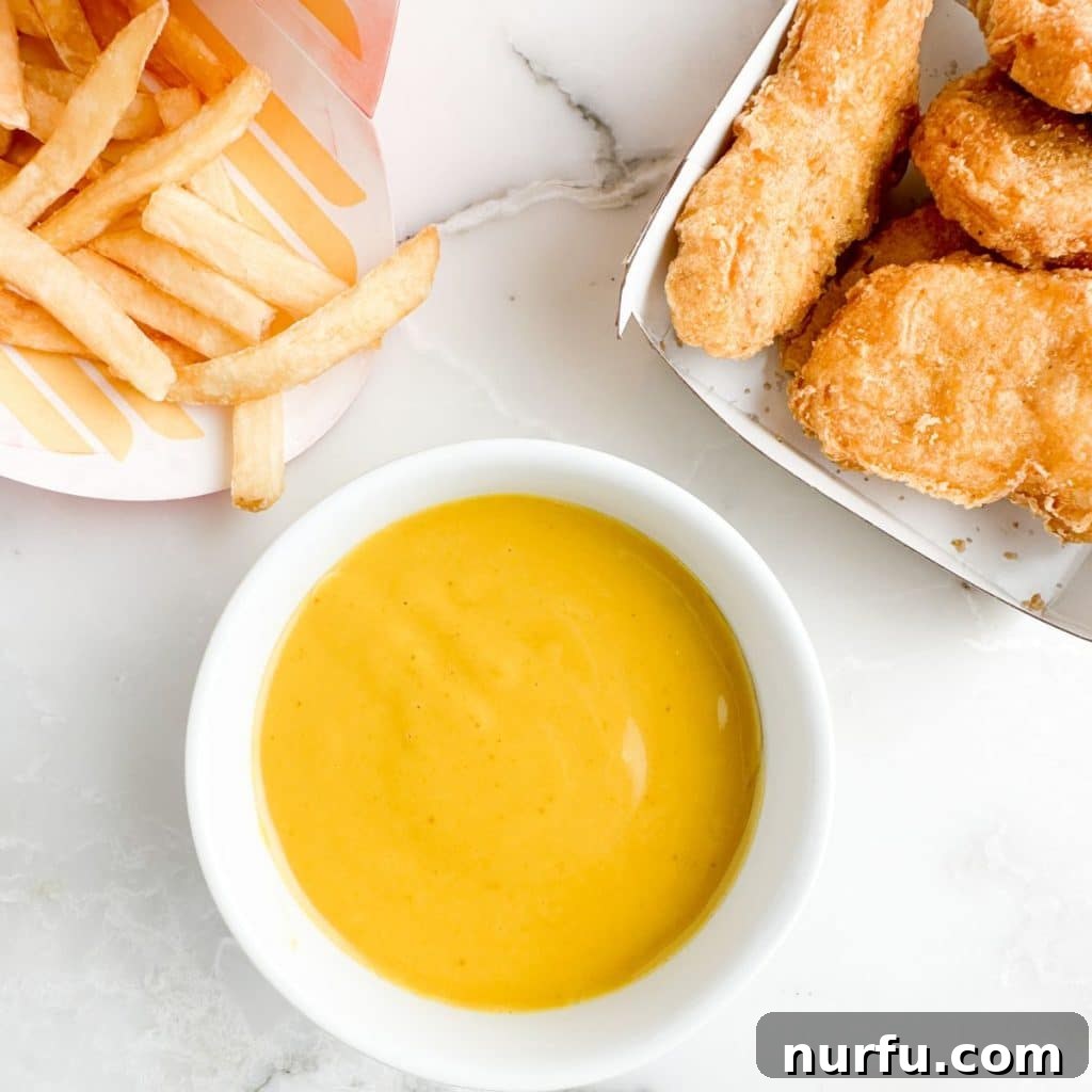 McDonald's Hot Mustard Sauce Copycat Recipe 5 A rustic wooden board featuring a bowl of golden hot mustard sauce, surrounded by crispy chicken nuggets and perfectly golden french fries, ready for dipping.