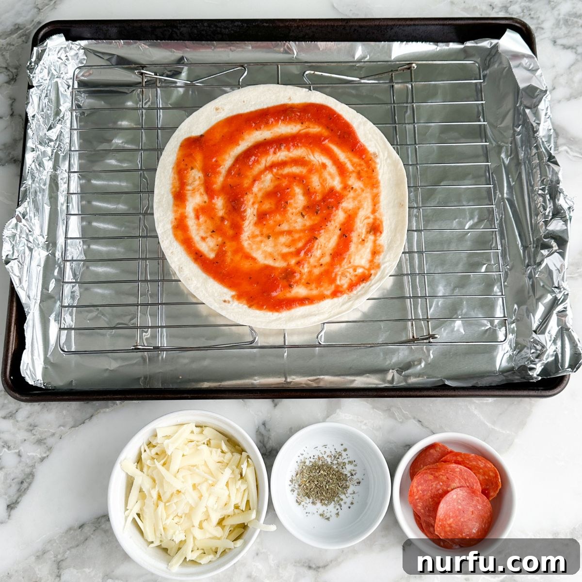 Effortless Tortilla Pizza 4 A flour tortilla sits on an oven-safe rack over a baking sheet, with a thin layer of rich pizza sauce expertly spread across its surface, ready for toppings.