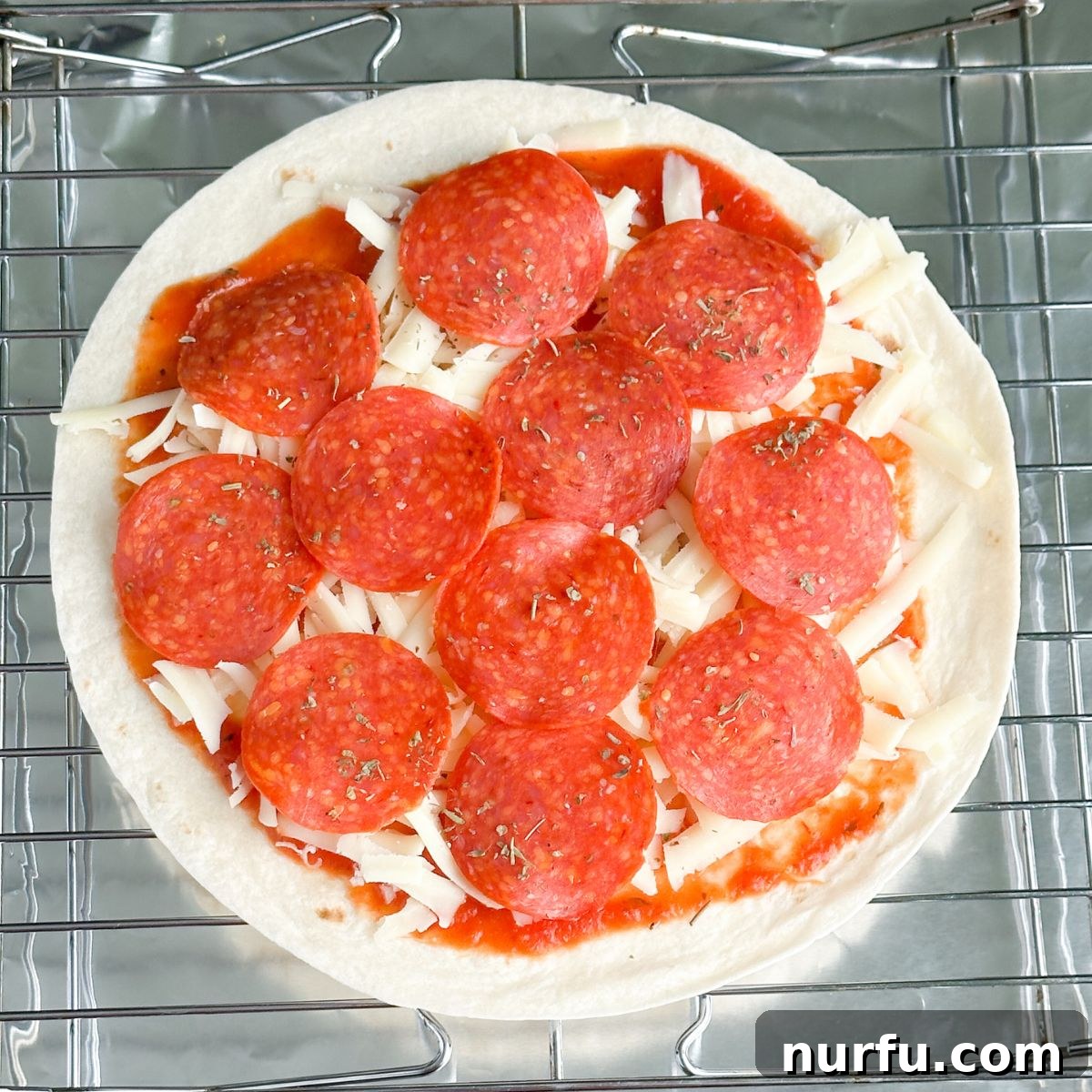 Effortless Tortilla Pizza 5 A prepared tortilla pizza on a baking sheet, generously topped with melted shredded cheese and savory pepperoni slices, poised for baking.
