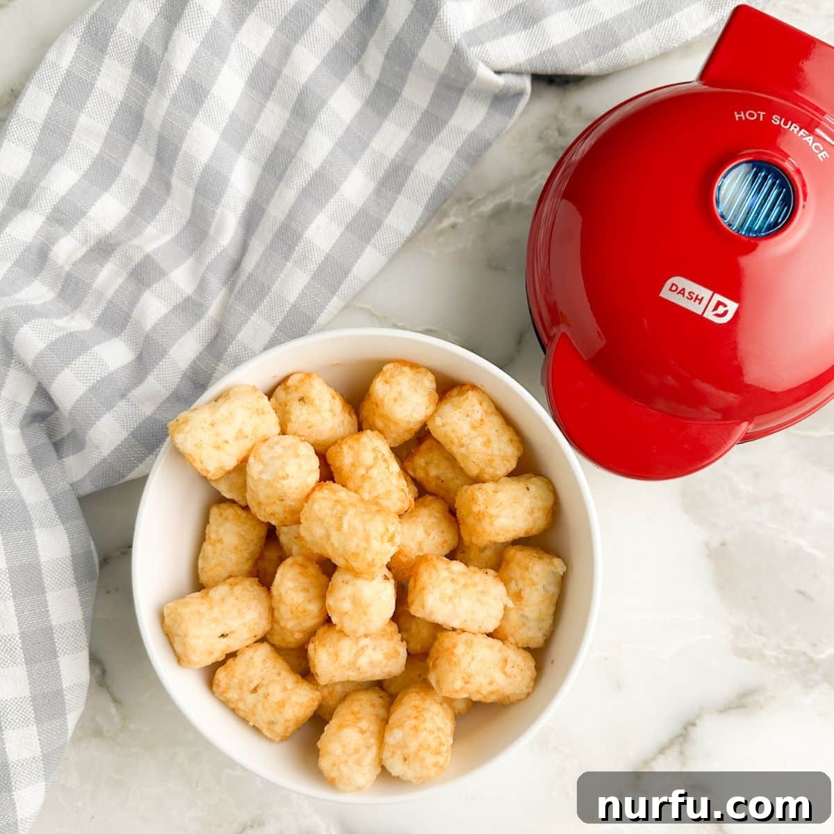 A bowl of thawed tater tots next to a vibrant red mini waffle maker, highlighting the simple ingredients needed for tater tot waffles.