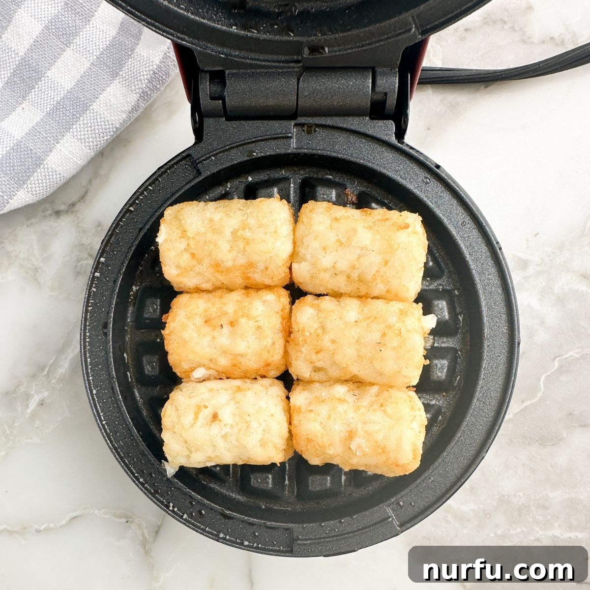 Tater tots cooking inside a waffle iron, showcasing the process of making tater tot waffles.