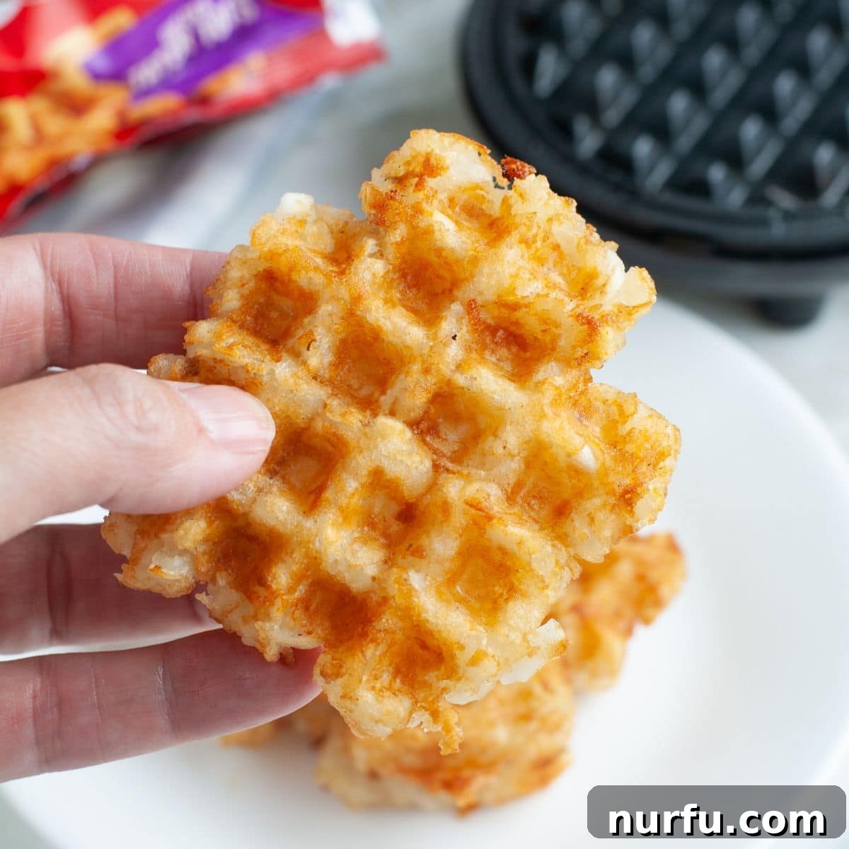 A hand holding a perfectly cooked, crispy tater tot waffle, showcasing its golden-brown texture.