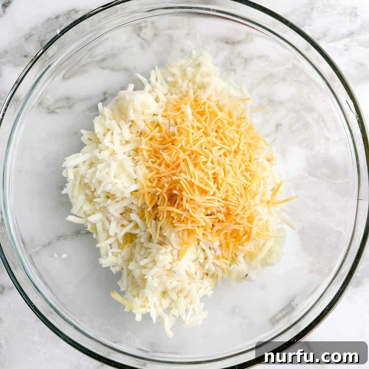 Crispy Waffle Hash Browns 4 A close-up view of a mixing bowl containing thawed hash browns and shredded cheddar cheese, ready to be combined.