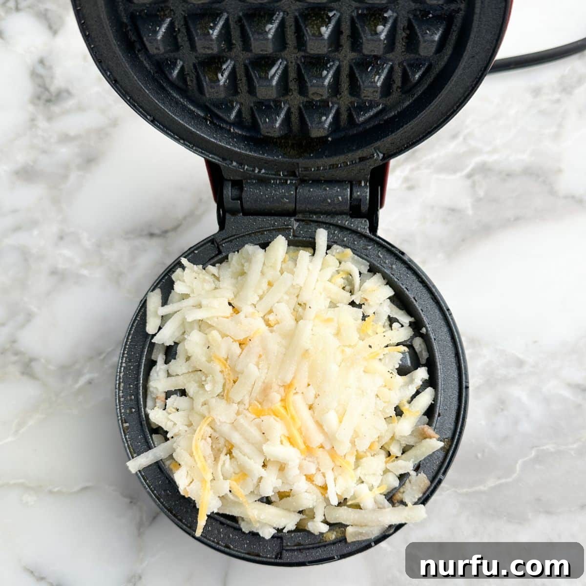 Crispy Waffle Hash Browns 5 The hash brown mixture, including shredded potatoes and cheese, actively cooking on a hot waffle iron, showing early signs of browning.