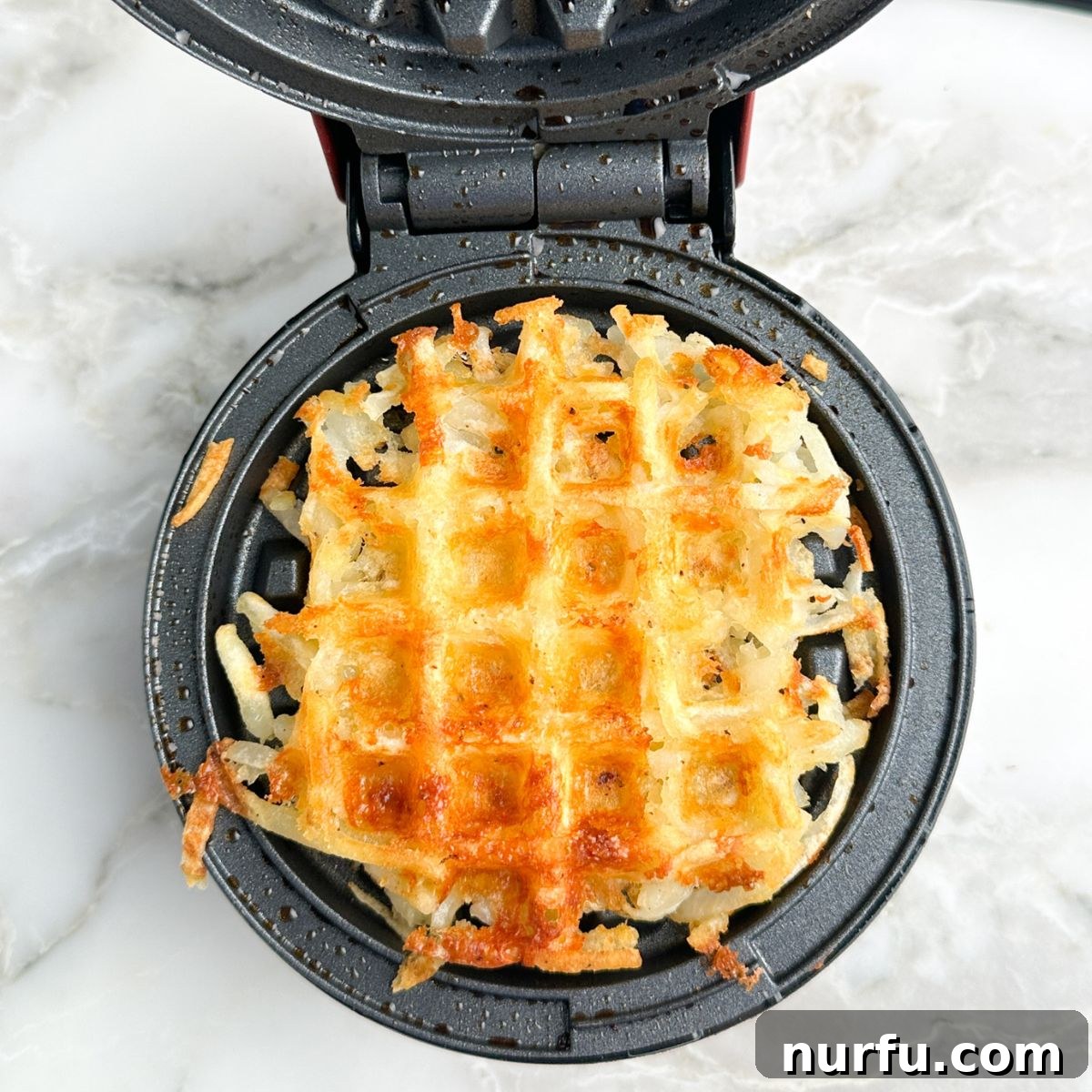 Crispy Waffle Hash Browns 6 A freshly cooked, golden-brown hash brown waffle still nestled in the grooves of the waffle iron, showcasing its crispy texture.