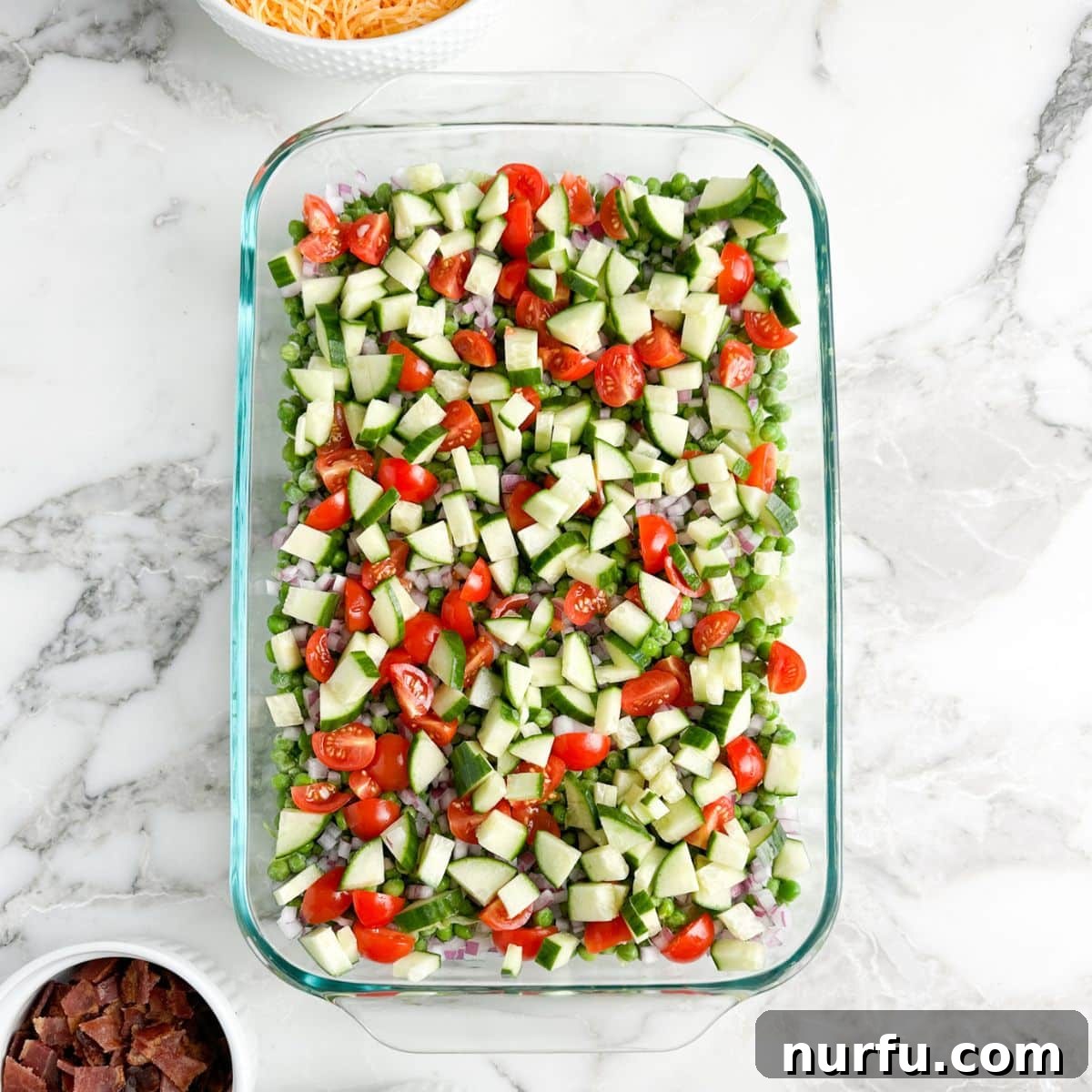 Layered Salad Perfection 5 A casserole dish showing the progression of the Seven Layer Salad, with layers of peas, onions, now topped with refreshing diced cucumbers and vibrant chopped tomatoes, building towards the final layers.