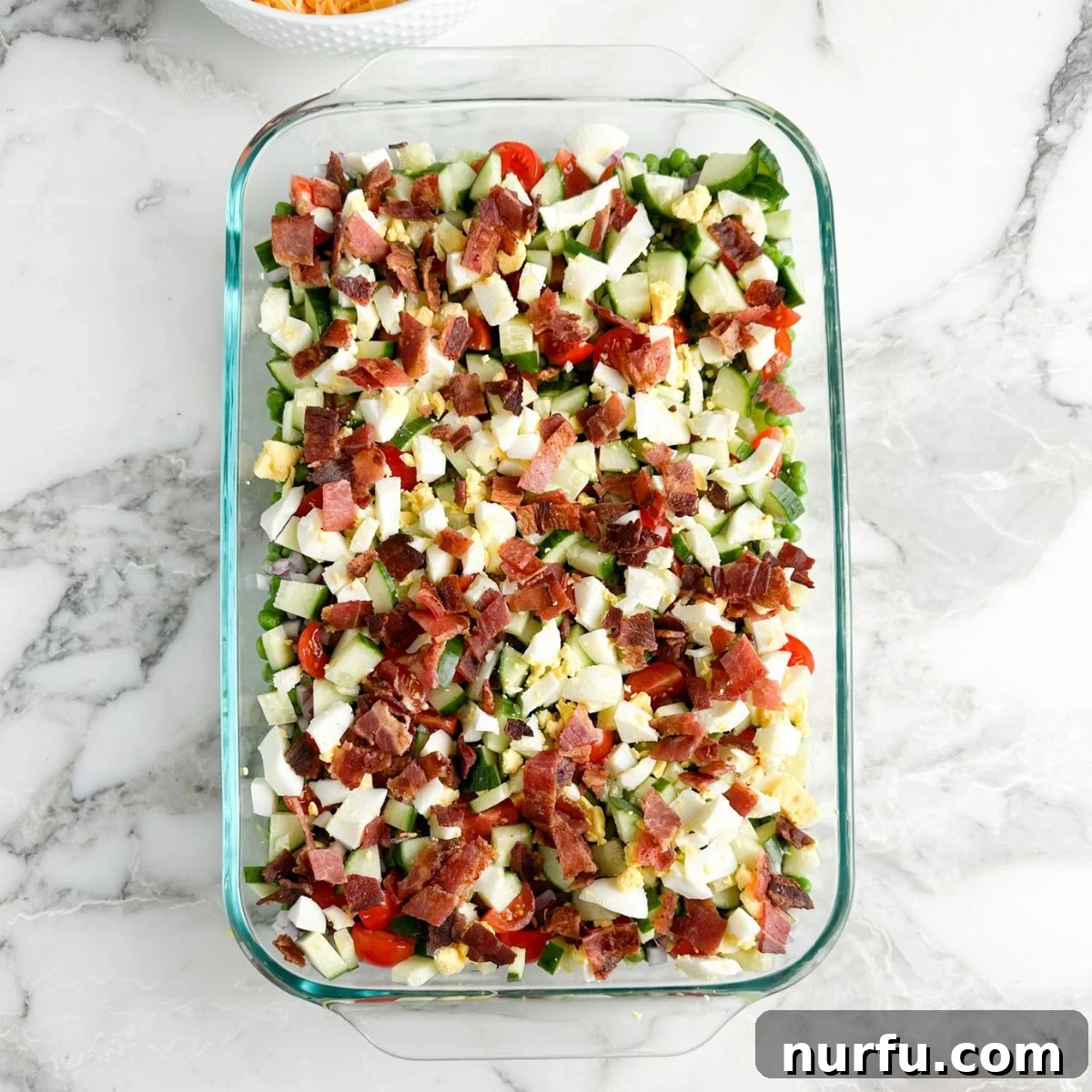Layered Salad Perfection 6 A casserole dish showcasing the nearly complete Seven Layer Salad with savory layers of chopped hard-boiled eggs and crispy bacon added over the fresh vegetables and lettuce base.