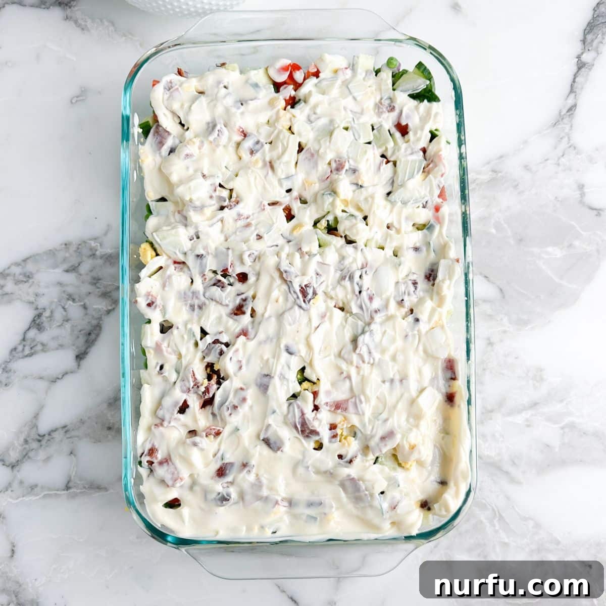 Layered Salad Perfection 7 A casserole dish with the Seven Layer Salad fully assembled, topped with a smooth, creamy layer of mayonnaise, ready for the final sprinkle of cheese before chilling.
