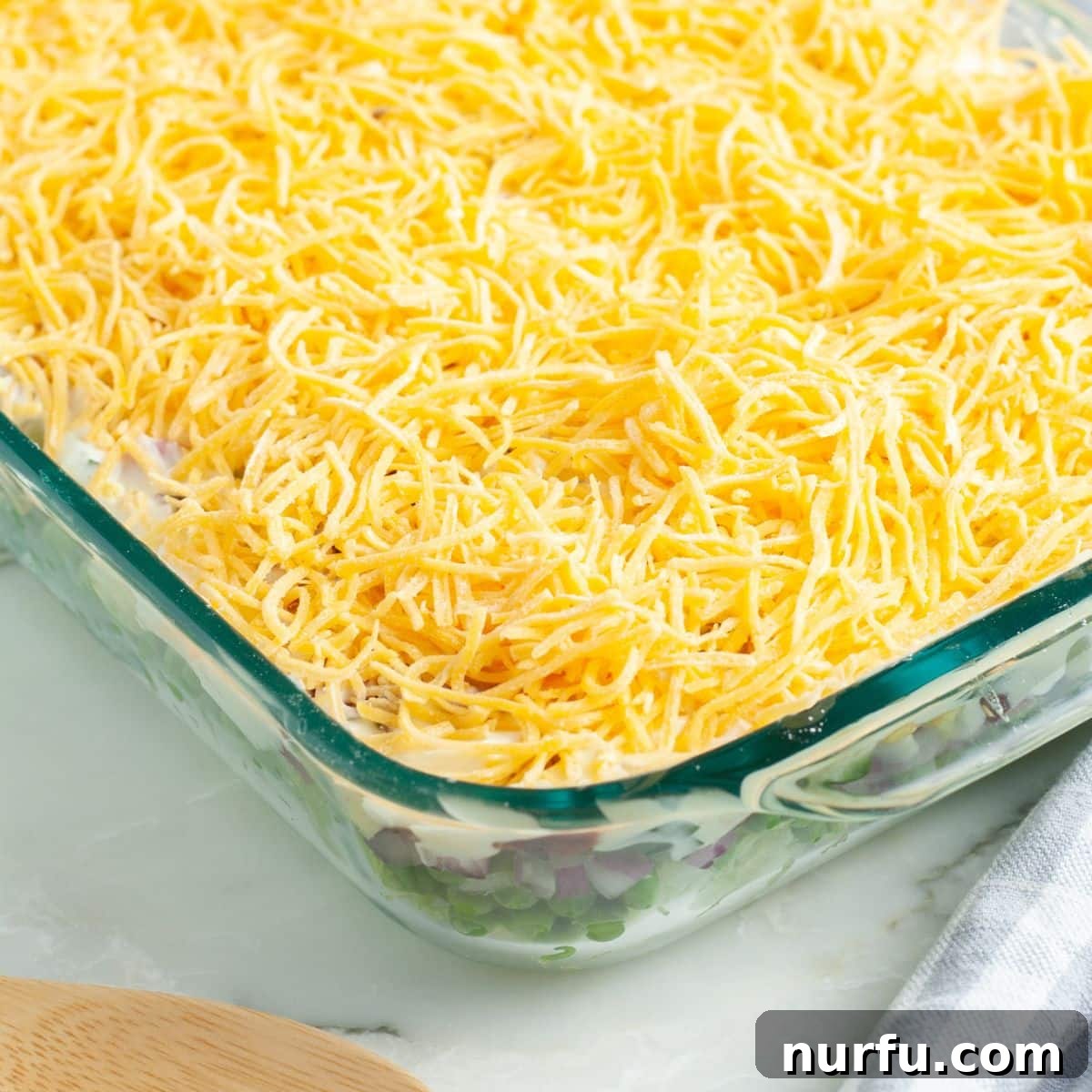 Layered Salad Perfection 8 A casserole dish with the completed Seven Layer Salad, generously topped with an even layer of shredded cheddar cheese, ready to be chilled and served.