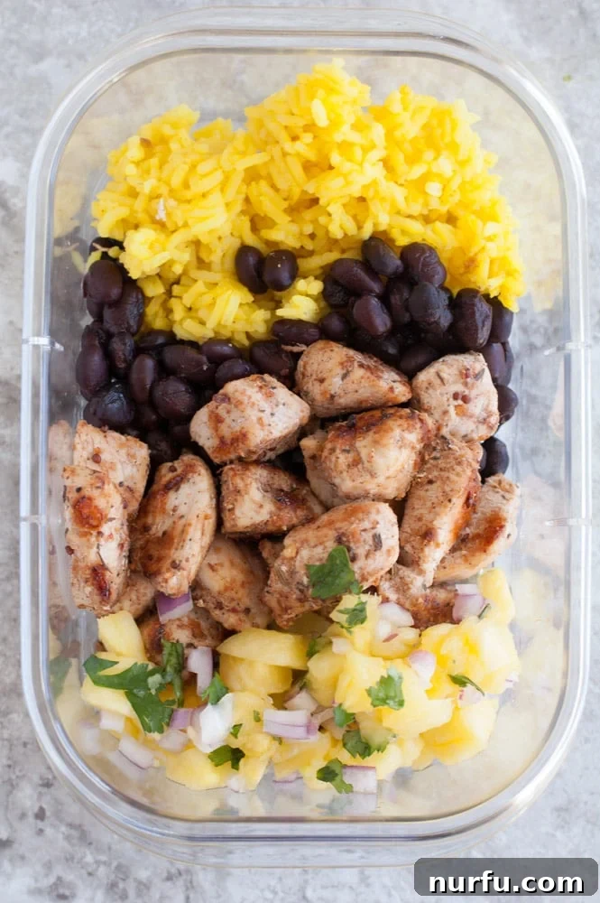 Rice, beans, chicken, pineapple salsa perfectly portioned in a container Close-up of a single Jerk Chicken Meal Prep Bowl showing rice, beans, chicken, and pineapple salsa.