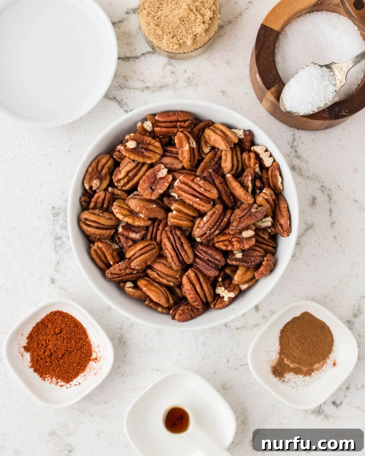 Perfectly Candied Pecans 3 A selection of raw ingredients including a bowl of pecan halves, brown sugar, ground cinnamon, vanilla extract, and cayenne pepper.