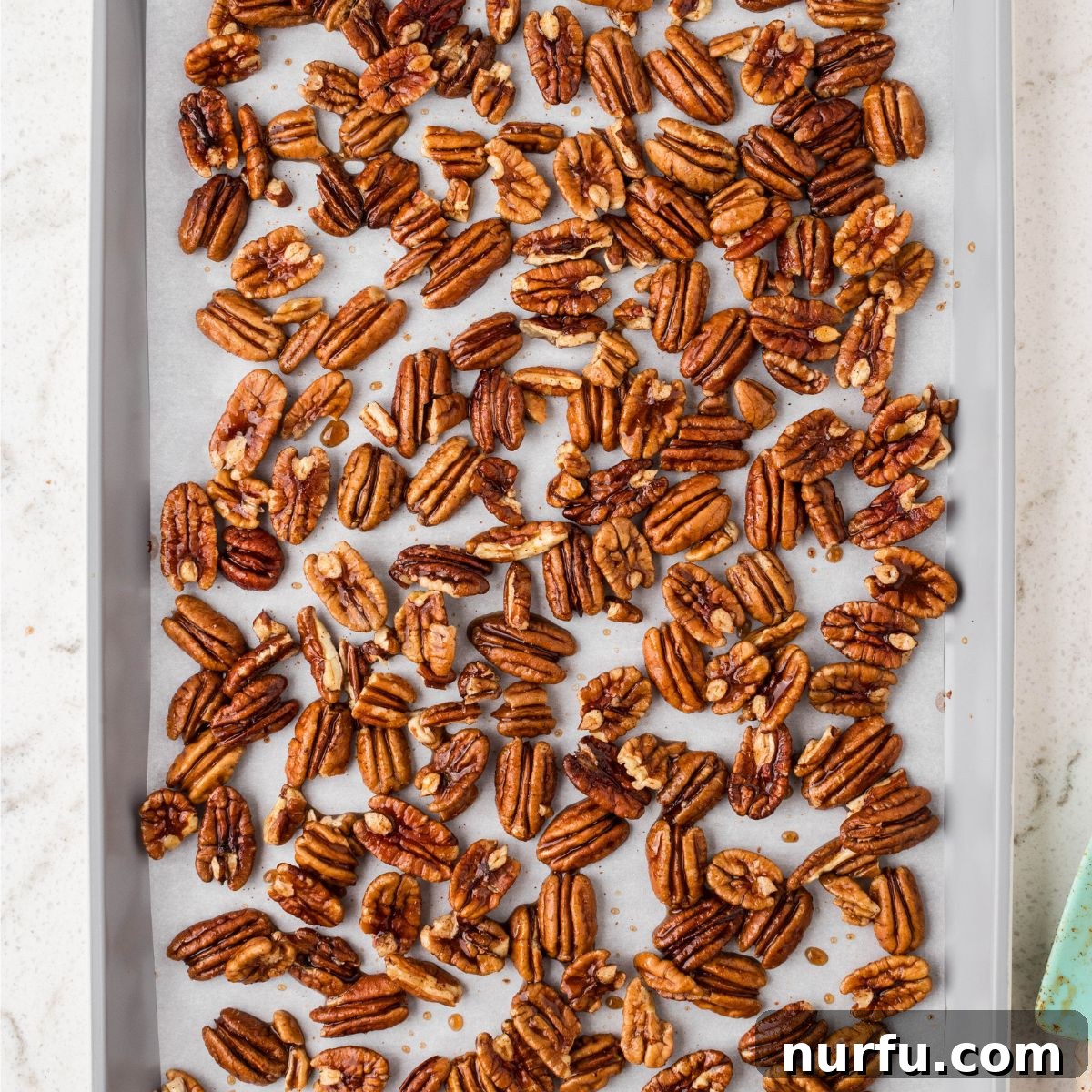 Perfectly Candied Pecans 6 Glazed pecans spread out in a single, even layer on a parchment-lined baking sheet, ready for baking.