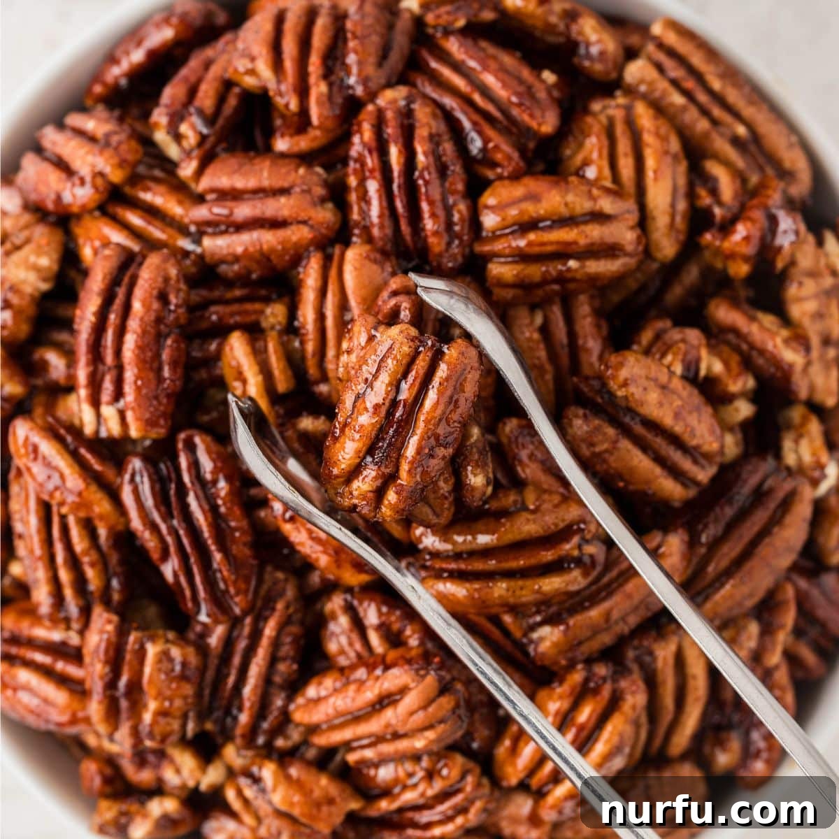 Perfectly Candied Pecans 7 A bowl filled with spiced glazed pecans, with a pair of tongs resting on the side, inviting to be picked up.