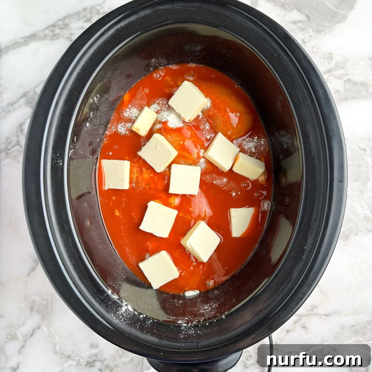 Effortless Slow Cooker Buffalo Chicken 5 Slow cooker with chicken, buffalo sauce, and pats of butter.