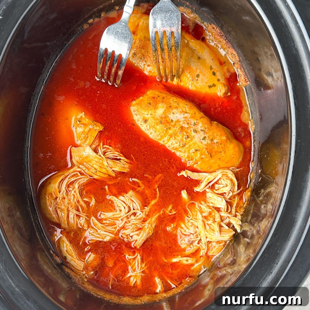 Effortless Slow Cooker Buffalo Chicken 6 Slow cooker with cooked buffalo chicken being shredded with two forks.