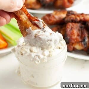 Jar with blue cheese sauce and chicken wing being dipped.