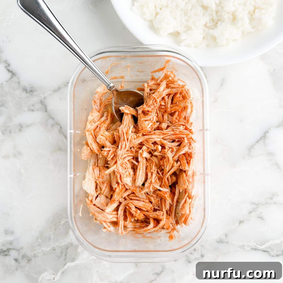 Fiery Buffalo Chicken Bowls 4 Shredded chicken in a container with buffalo sauce and a spoon.