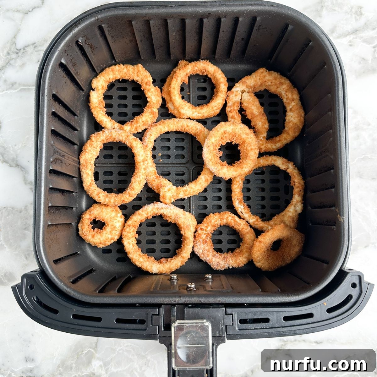 Crispy Alexia Onion Rings in the Air Fryer 4 Frozen Alexia onion rings neatly arranged in a single layer in an air fryer basket, ready to be cooked.