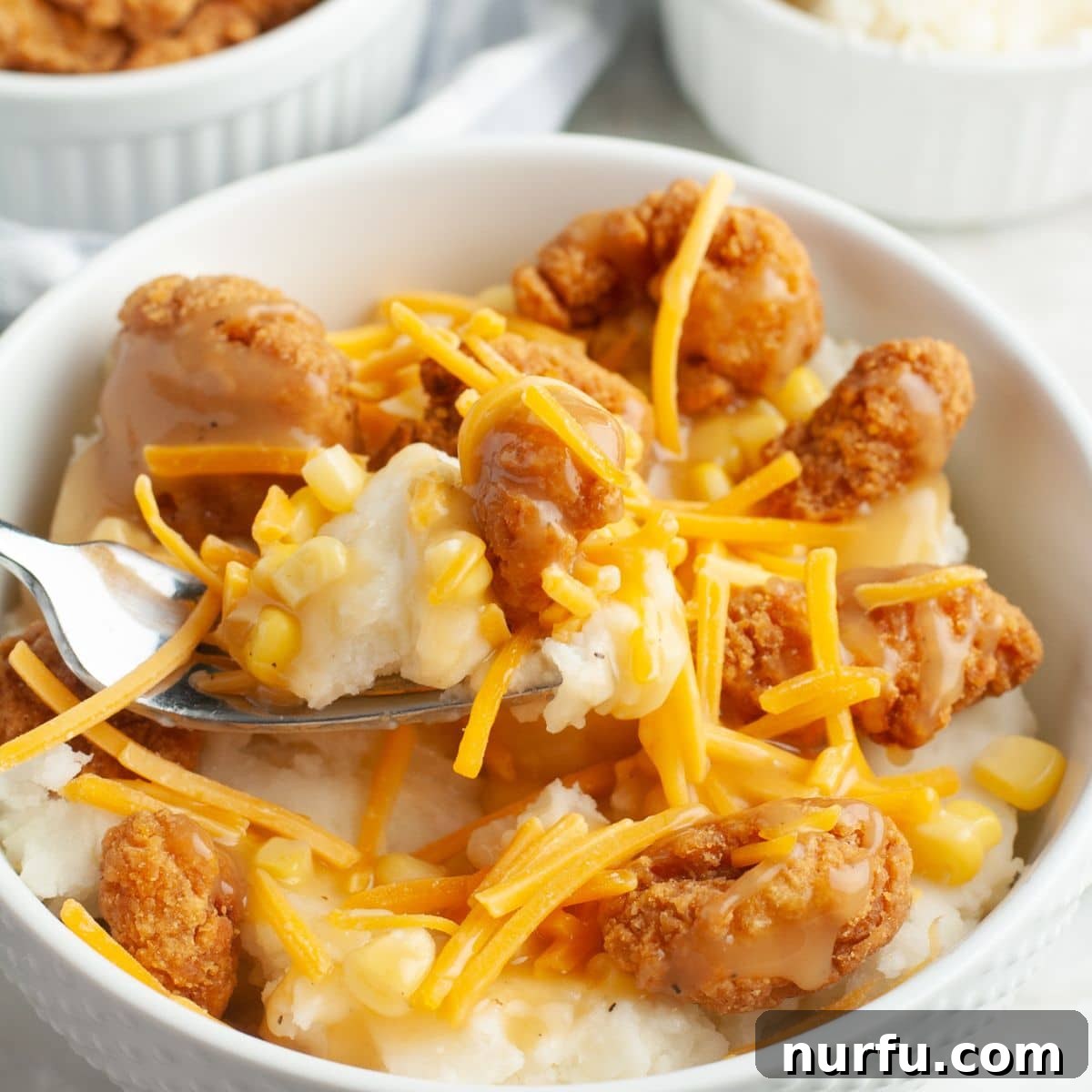 Homemade Crispy Chicken & Gravy Bowl 2 A hearty bowl featuring crispy fried chicken, fluffy mashed potatoes, and a topping of shredded cheddar cheese, all drizzled with savory gravy.
