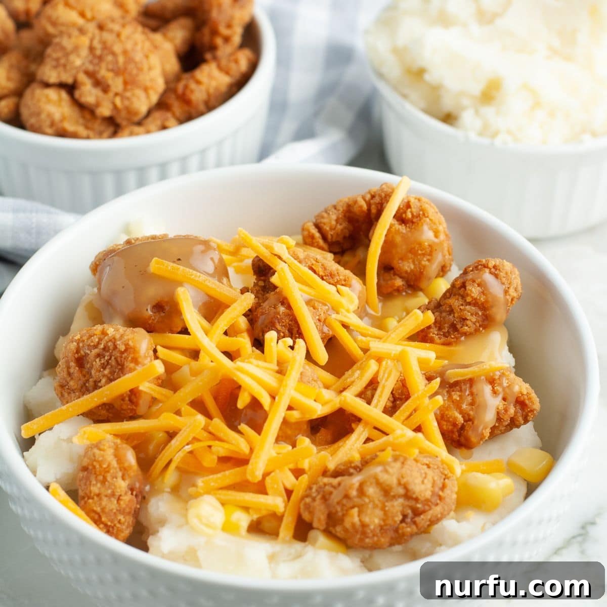 Homemade Crispy Chicken & Gravy Bowl 5 A close-up shot of a single KFC Famous Bowl, showcasing the layers of mashed potatoes, crispy popcorn chicken, and melted shredded cheese.