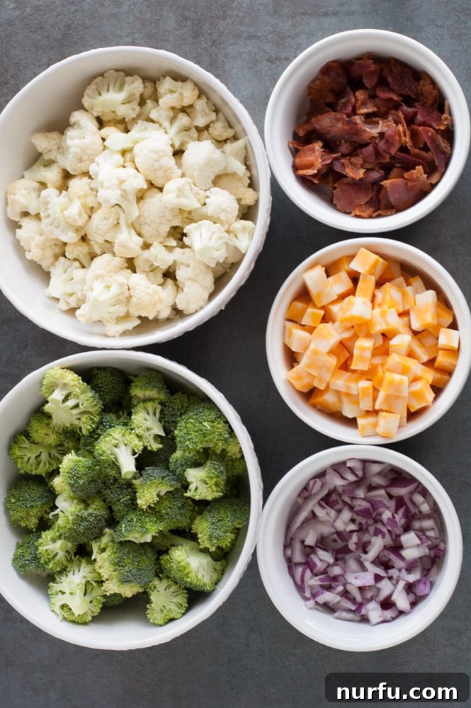 Broccoli Cauliflower Salad with bacon A bowl filled with the raw components of the salad: vibrant broccoli and cauliflower florets, crisp bacon pieces, rich cheese cubes, and finely diced red onion, ready to be dressed.