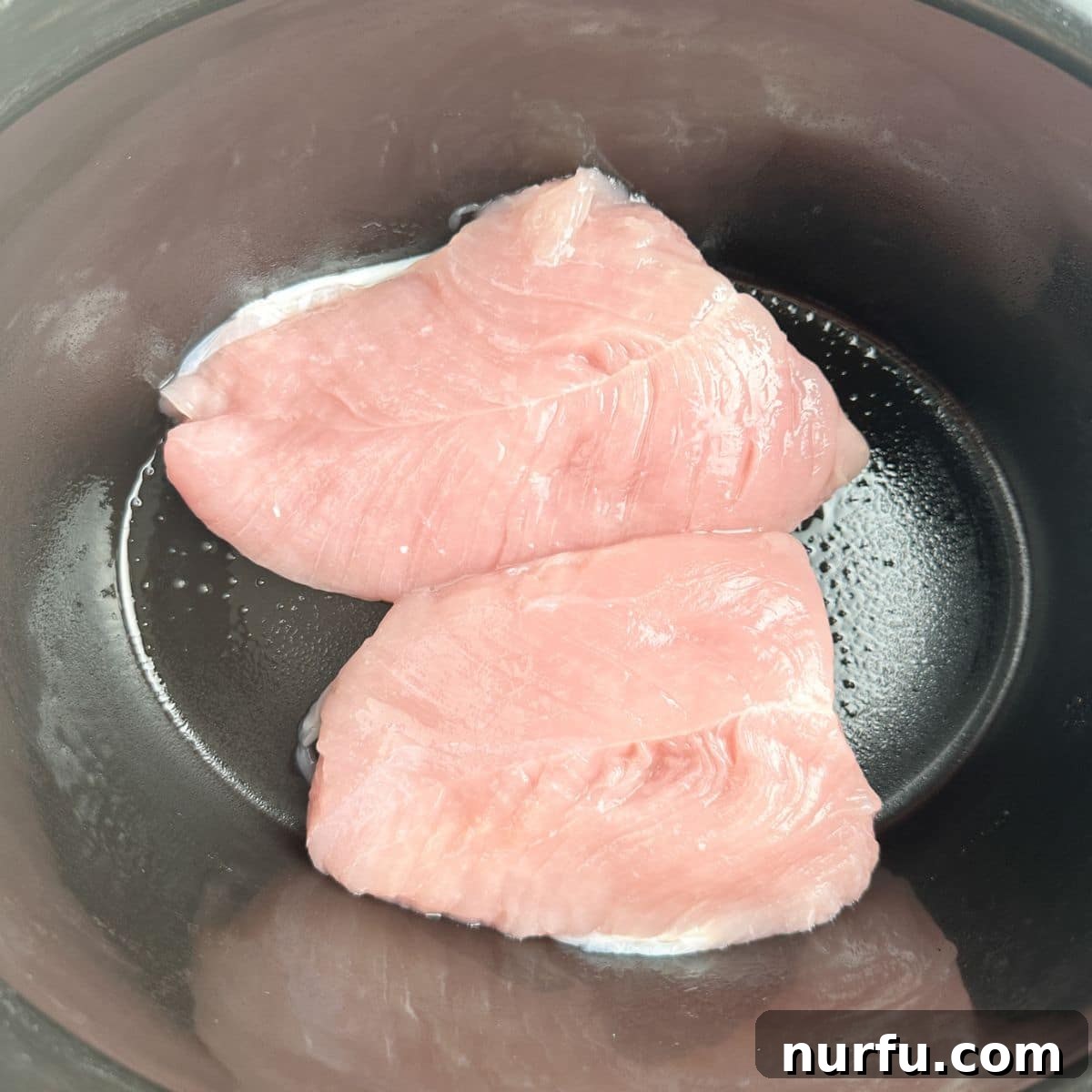 Two turkey tenderloins neatly arranged in the base of a slow cooker, ready for cooking.