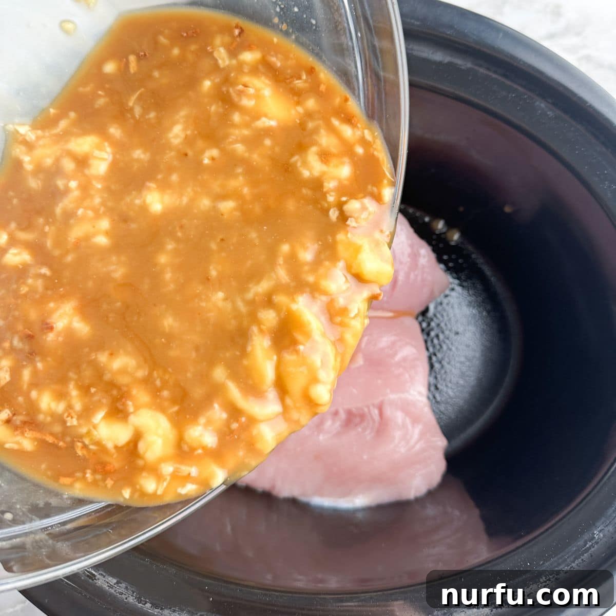 A bowl of creamy onion soup mixture being poured over turkey tenderloins in a slow cooker, ensuring even coating.