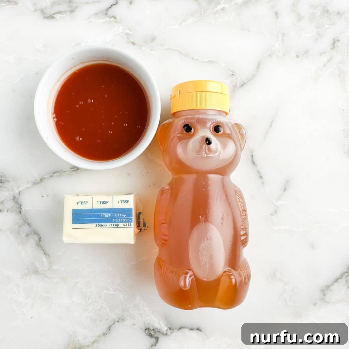 Bowl of hot sauce, butter, and honey bear container.
