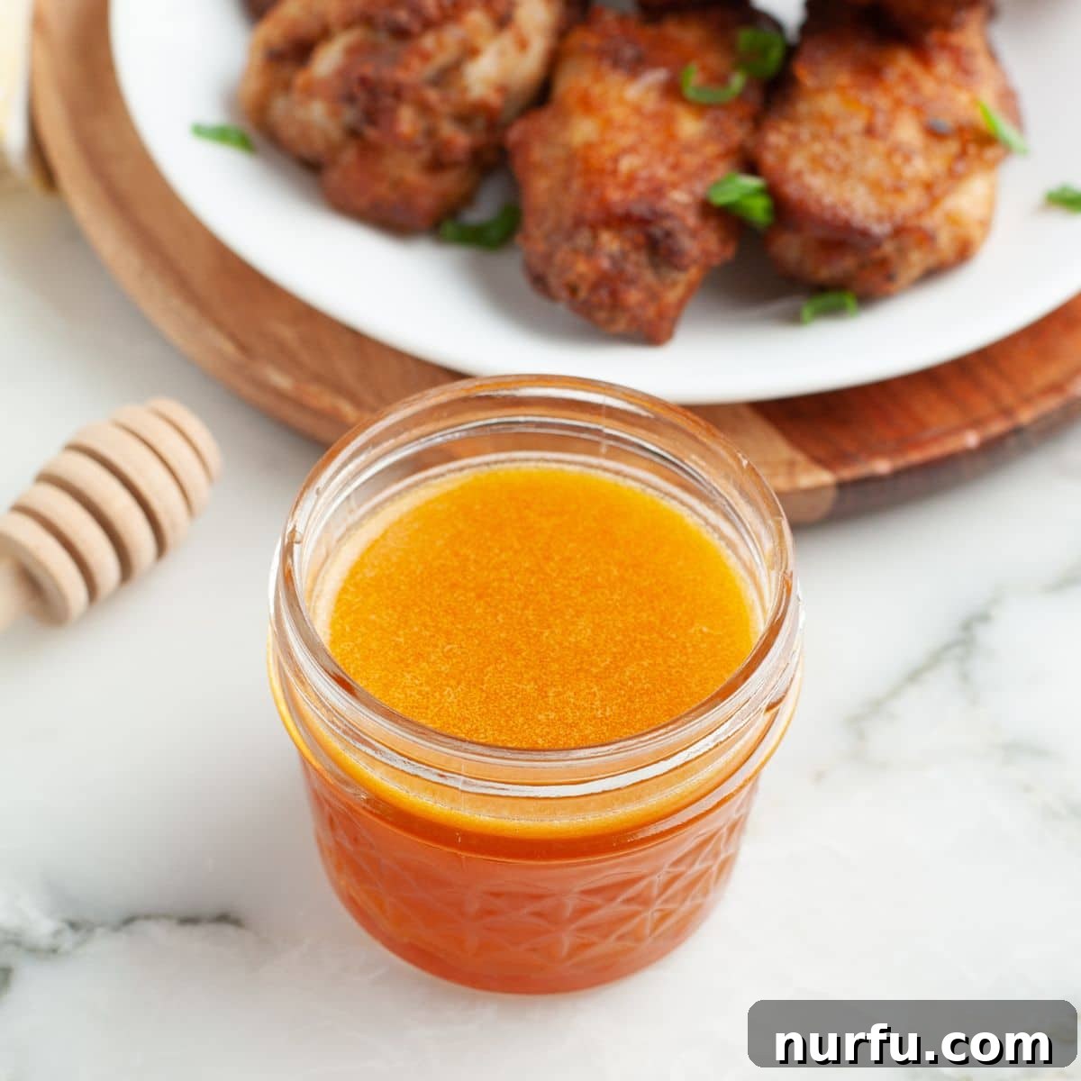 Jar of hot honey wing sauce with a plate of wings.