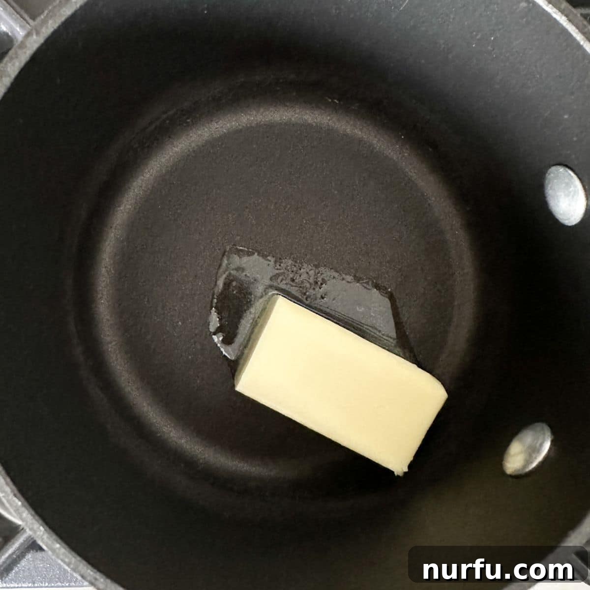 Zesty Lemon Pepper Sauce 4 A small saucepan on a stovetop with butter slowly melting, indicating the initial step of preparing the lemon pepper sauce.