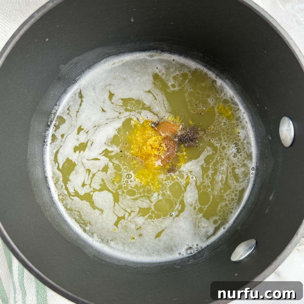 Zesty Lemon Pepper Sauce 5 A saucepan filled with melted butter, to which fresh lemon zest and ground black pepper have just been added, awaiting a whisk to combine the ingredients into a harmonious sauce.