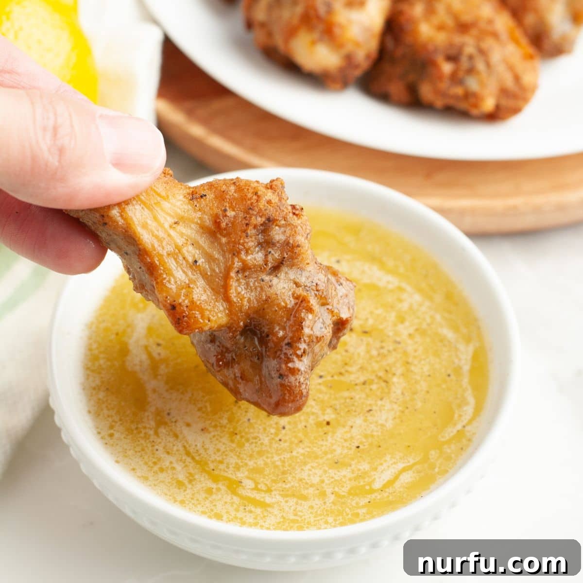 Zesty Lemon Pepper Sauce 6 A golden-brown chicken wing being dipped into a bowl of homemade lemon pepper sauce, highlighting its perfect consistency and inviting appeal.