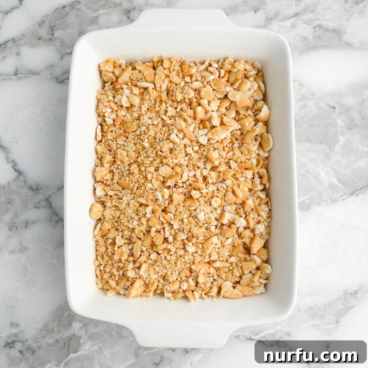 Tropical Pineapple Delight 6 A close-up view of a casserole dish, its pineapple and cheese filling now beautifully covered with an even, golden layer of buttery crushed cracker crumbs, patiently awaiting its transformation in the oven.