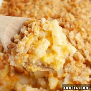 A wooden spoon with a generous serving of golden-brown pineapple casserole, showcasing its crispy topping and soft, creamy interior.