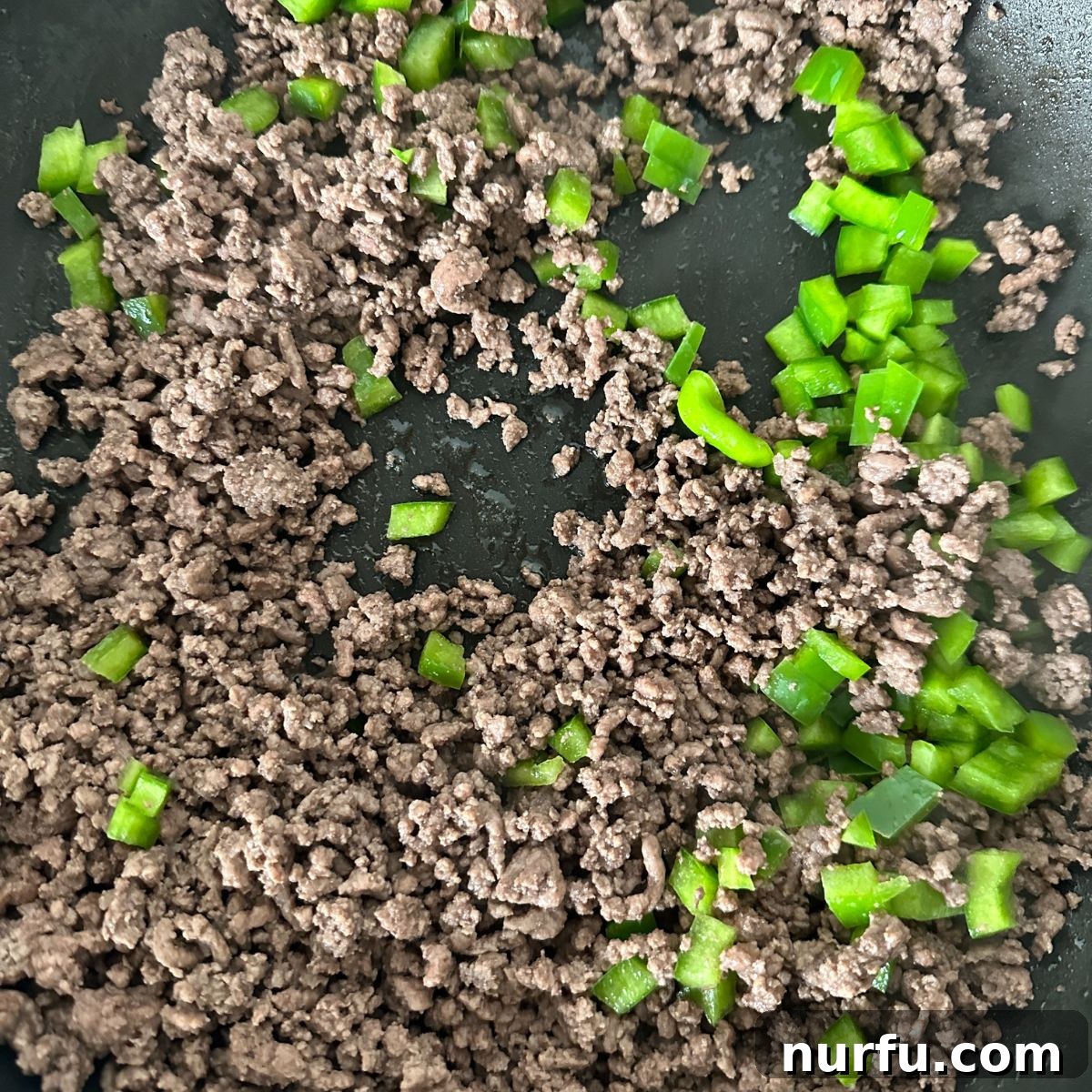 Ground beef and diced green bell pepper sizzling together in a skillet, creating the flavorful base for the casserole.