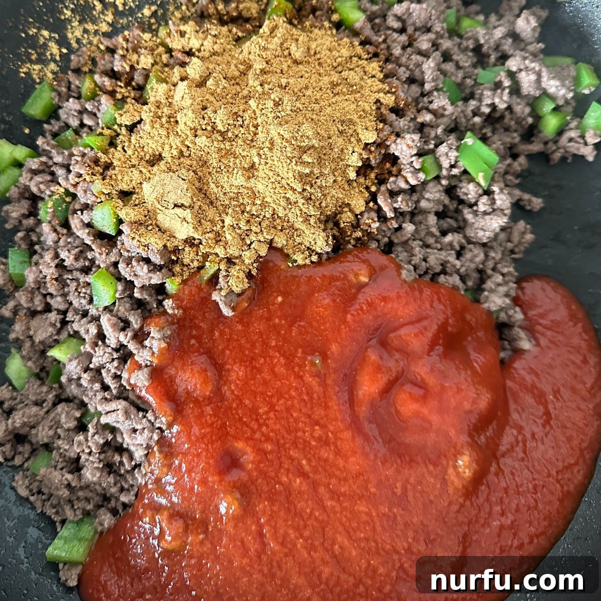 A savory blend of ground beef, taco seasonings, and rich tomato sauce simmering in a skillet, creating the flavorful heart of the Taco Twist Casserole.
