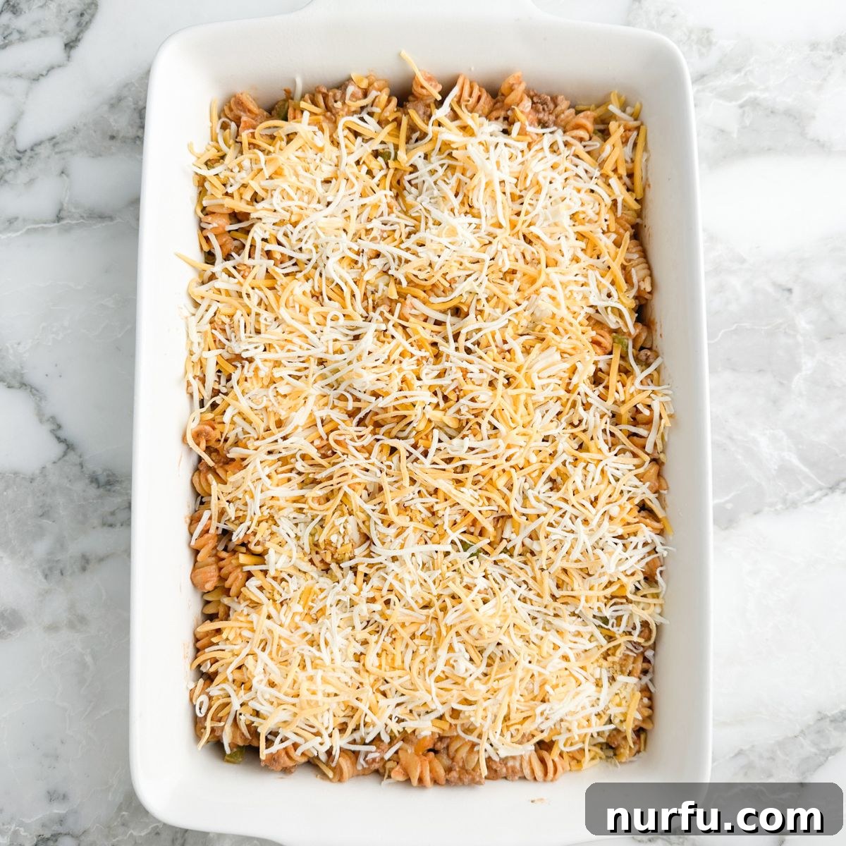 A casserole dish filled with a tantalizing pasta mixture, beautifully topped with a layer of shredded cheese, ready to be baked to melted perfection.