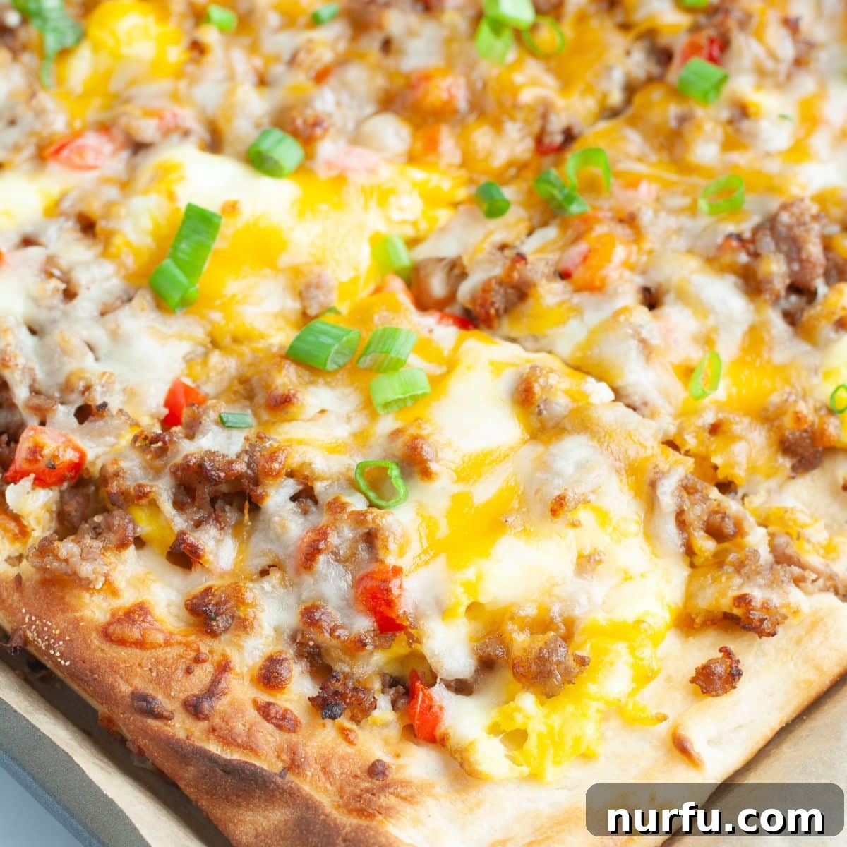 Hand holding a slice of breakfast pizza, showcasing the toppings of eggs, sausage, and melted cheese on a golden crust.