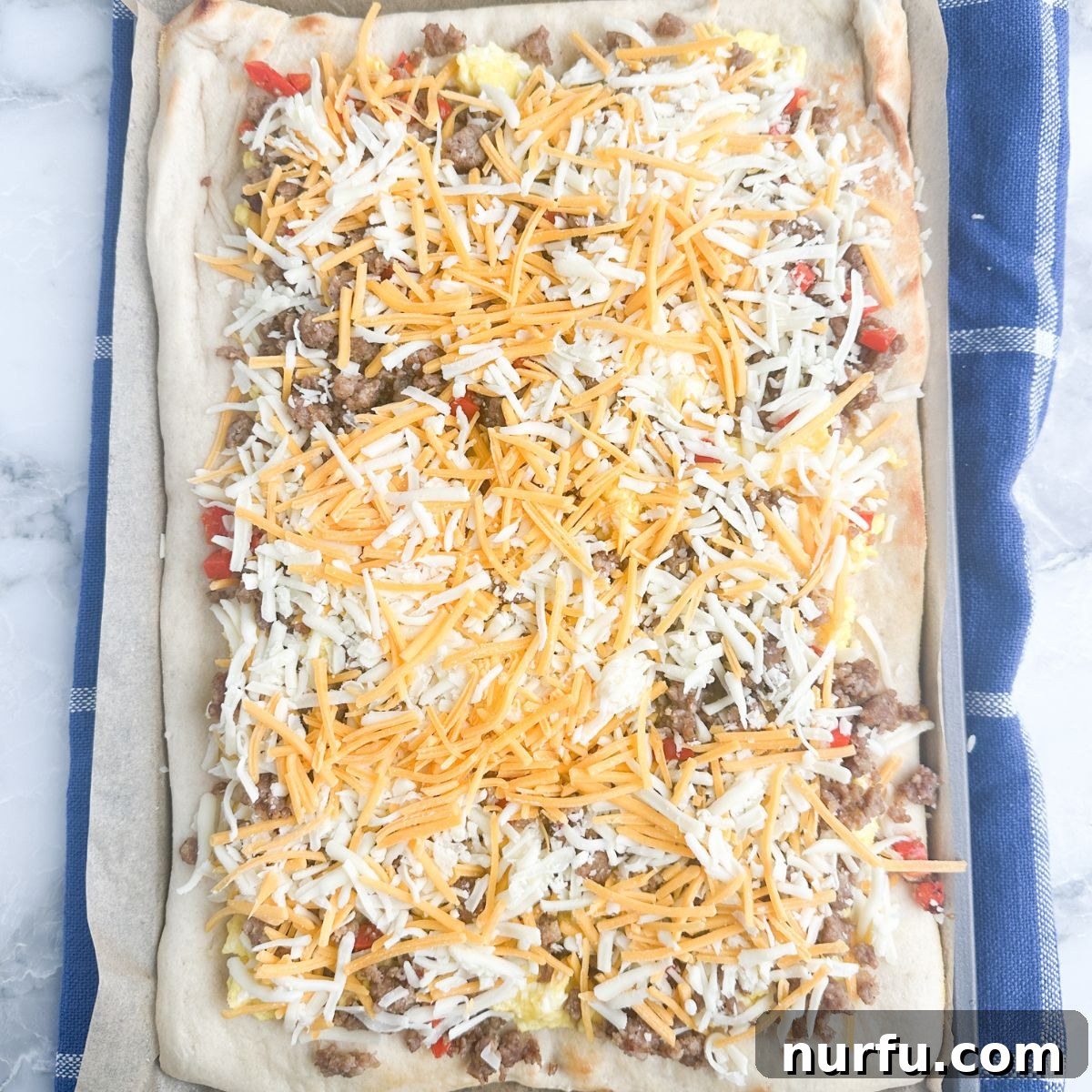 A fully assembled breakfast pizza with a golden crust, fluffy eggs, savory sausage, and perfectly melted shredded cheese, fresh out of the oven.